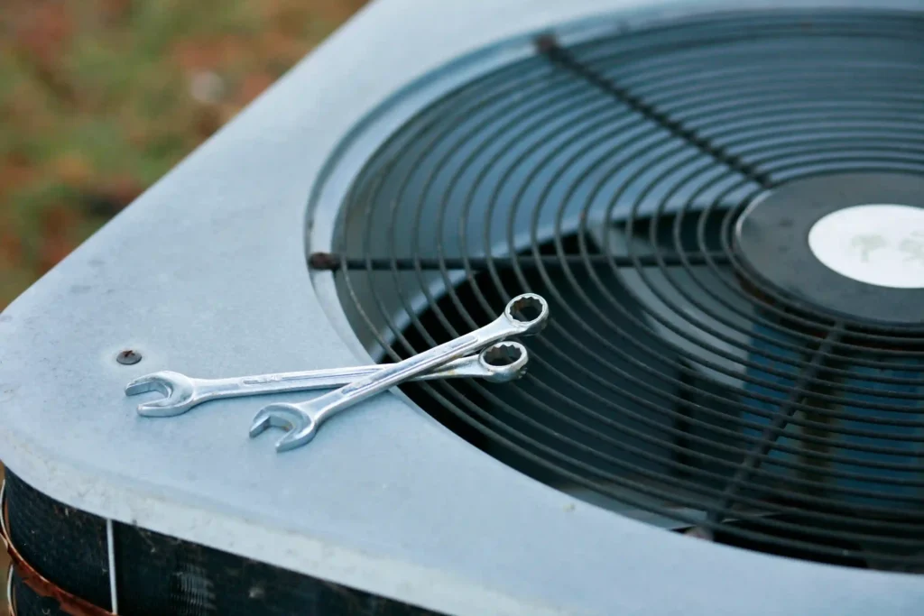 Two wrenches resting on the fan grille of an outdoor air conditioning unit, symbolizing HVAC repair and maintenance tools.
