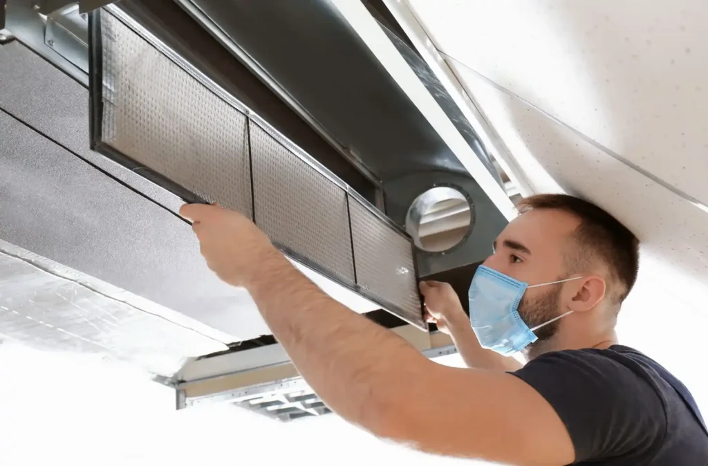 Person replacing a dirty air filter in a ceiling-mounted HVAC system for improved indoor air quality and energy efficiency