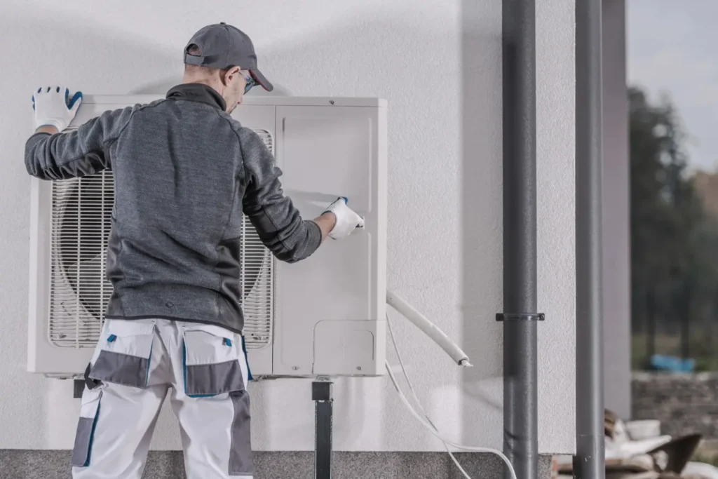 A man replacing a heat Pump installed in the wall of a house