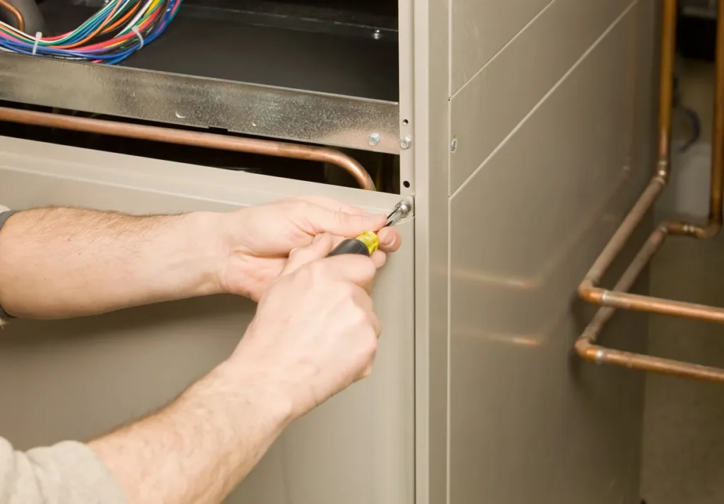 Technician using a screwdriver to adjust the side panel of an HVAC unit with visible copper pipes and electrical wiring during maintenance
