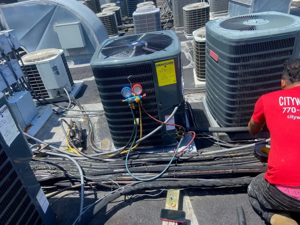 Technician servicing rooftop air conditioning units with gauges and hoses.